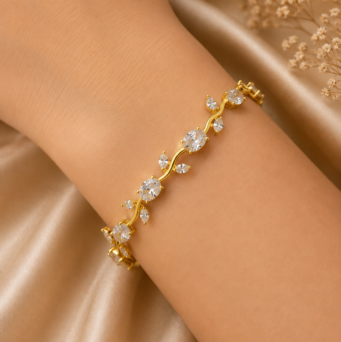 A delicate gold vine bracelet with clear gemstones, worn on a woman's wrist against a soft beige satin background.
