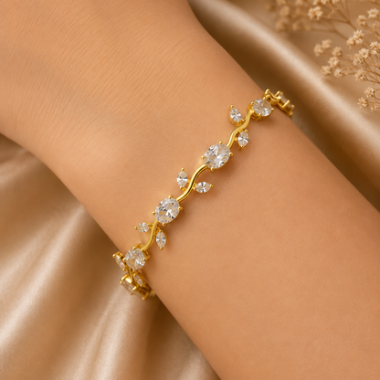 A delicate gold vine bracelet with clear gemstones, worn on a woman's wrist against a soft beige satin background.