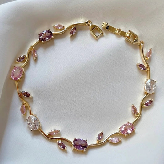 Gold bracelet with pink and clear gemstones on a white background