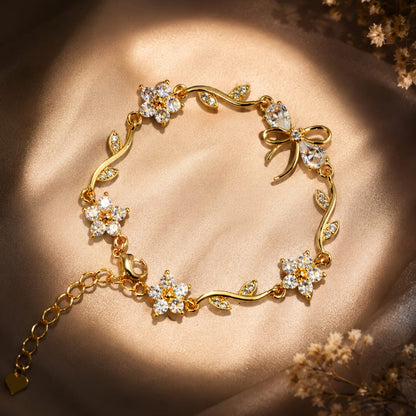 A gold bracelet with floral and vine motifs set with clear crystals, displayed on a draped beige satin fabric with warm sunlight and dried flowers in the corners.
