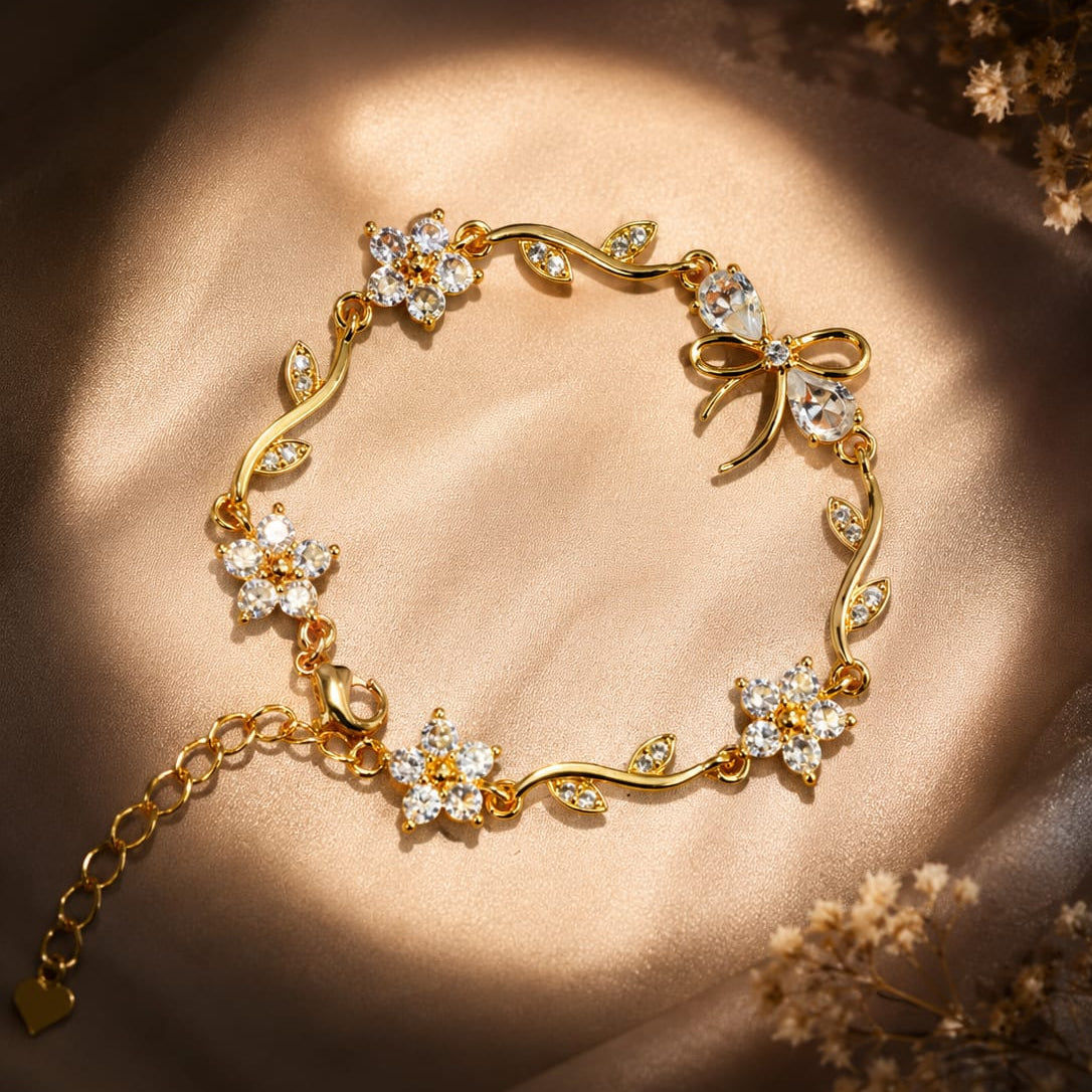 A gold bracelet with floral and vine motifs set with clear crystals, displayed on a draped beige satin fabric with warm sunlight and dried flowers in the corners.