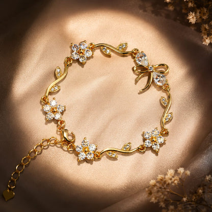 A gold bracelet with floral and vine motifs set with clear crystals, displayed on a draped beige satin fabric with warm sunlight and dried flowers in the corners.