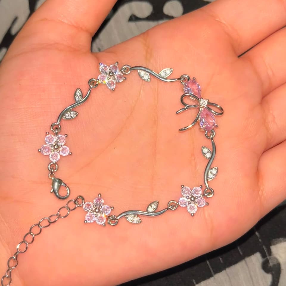 A silver-toned bracelet with pink crystal flowers and bow details, displayed on an open hand.