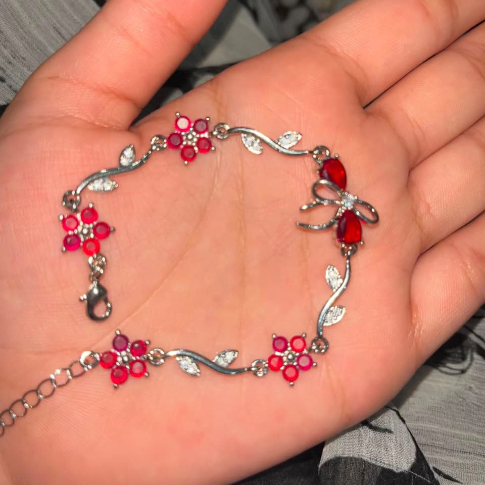 A silver-toned bracelet with red flower and bow motifs, displayed on an open hand.