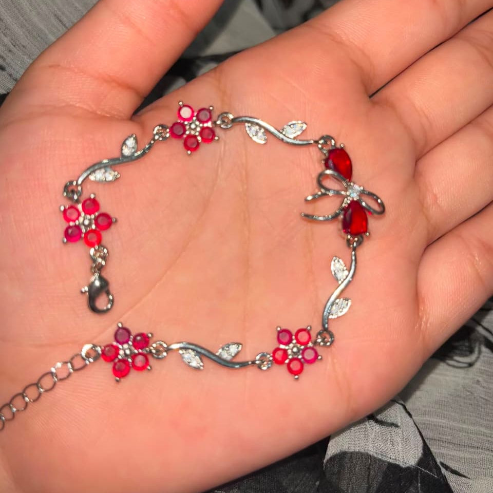 A silver-toned bracelet with red flower and bow motifs, displayed on an open hand.
