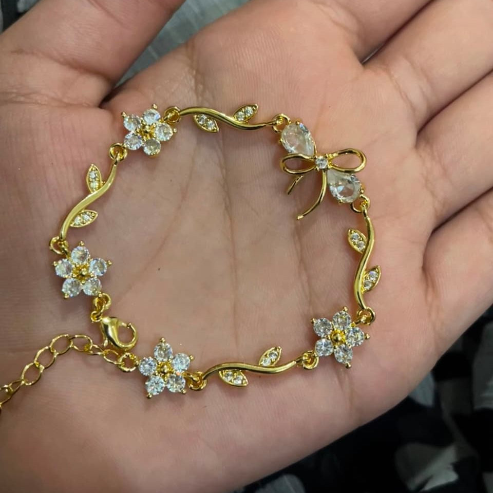A gold bracelet with clear crystal flowers and leaves, displayed on an open hand.