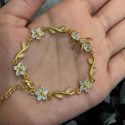 A gold bracelet with clear crystal flowers and leaves, displayed on an open hand.
