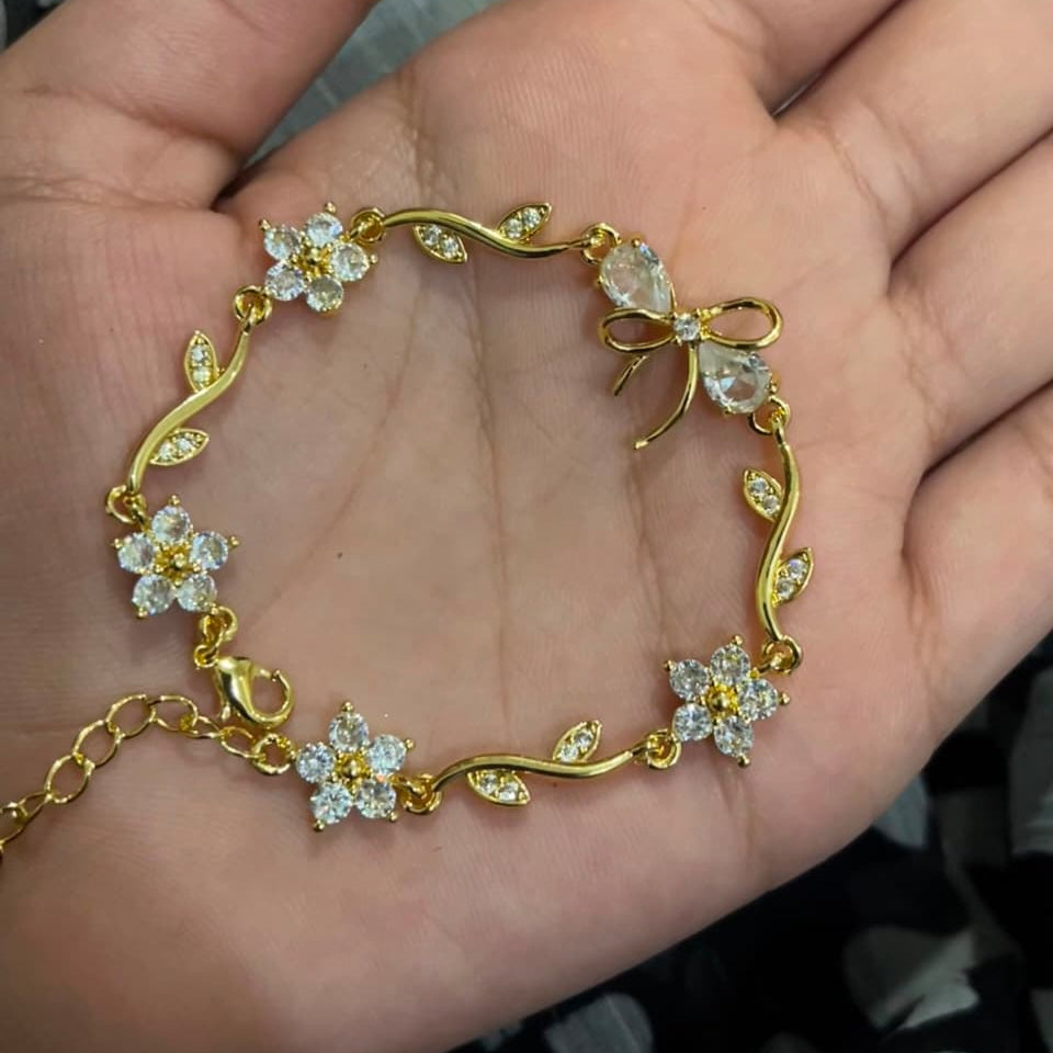 A gold bracelet with clear crystal flowers and leaves, displayed on an open hand.