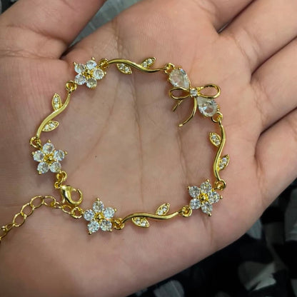 A gold bracelet with clear crystal flowers and leaves, displayed on an open hand.