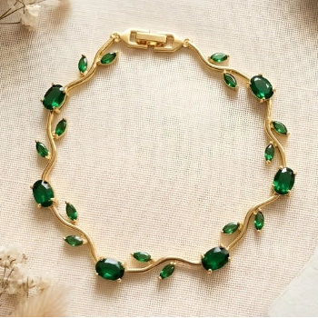 Gold bracelet with green gemstones on a textured surface with decorative elements.