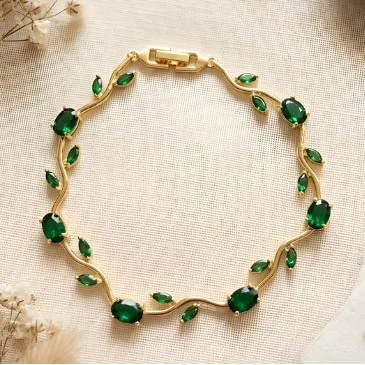 Gold bracelet with green gemstones on a textured surface with decorative elements.